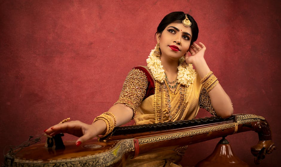 Elegant Indian woman in traditional wear posing with a Veena against a red backdrop.